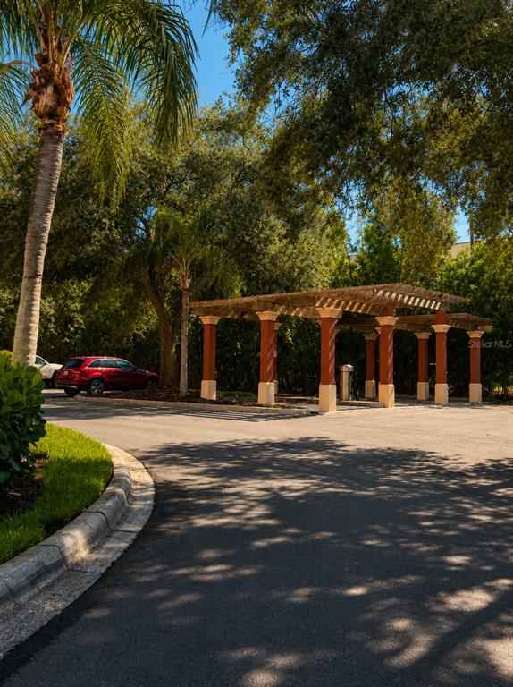 A wooden pergola with red columns stands in a parking area near trees — 2717 VIA CIPRIANI UNIT 631A, CLEARWATER, FL