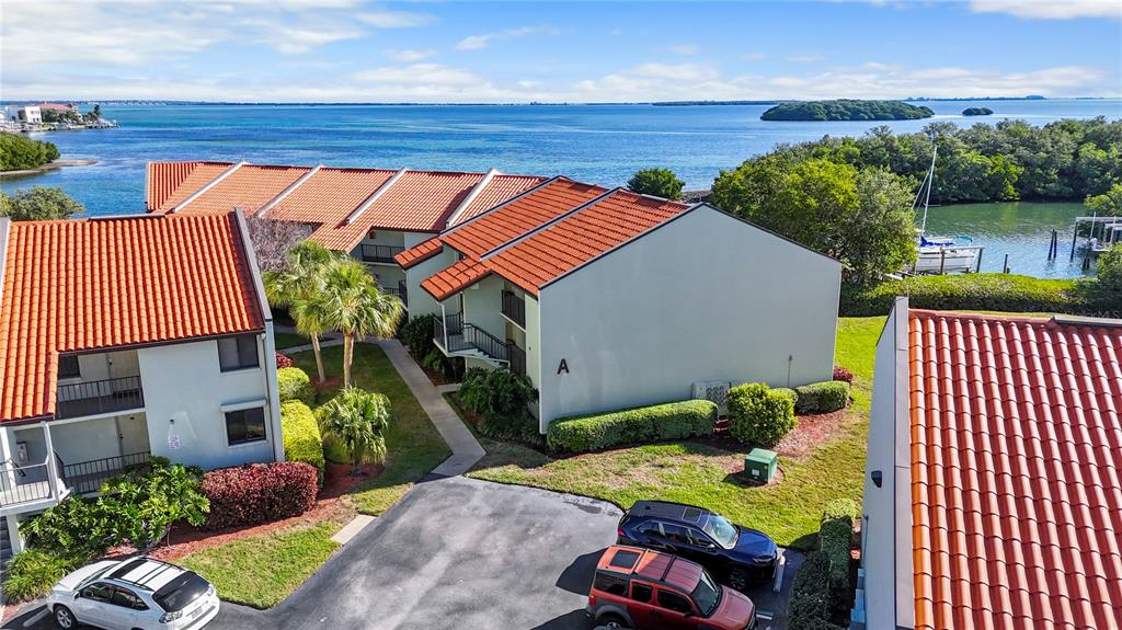 An aerial view shows multi-story apartment buildings with orange tile roofs near a coastal waterway — 1515 PINELLAS BAYWAY S UNIT 7, TIERRA VERDE, FL