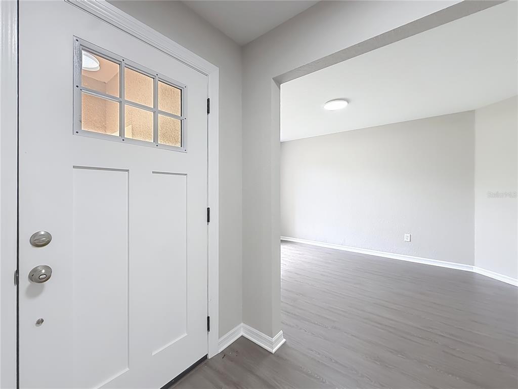 A white front door with a window opens into a room with gray wood flooring — 213 LINDER DRIVE, HOMOSASSA, FL