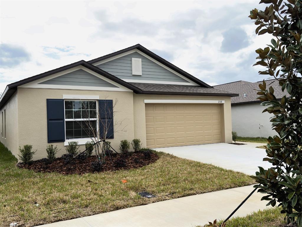 A single-story house with a tan stucco exterior, dark blue shutters, and a two-car garage — 2318 ALLIUM ROSEUM LANE, PLANT CITY, FL