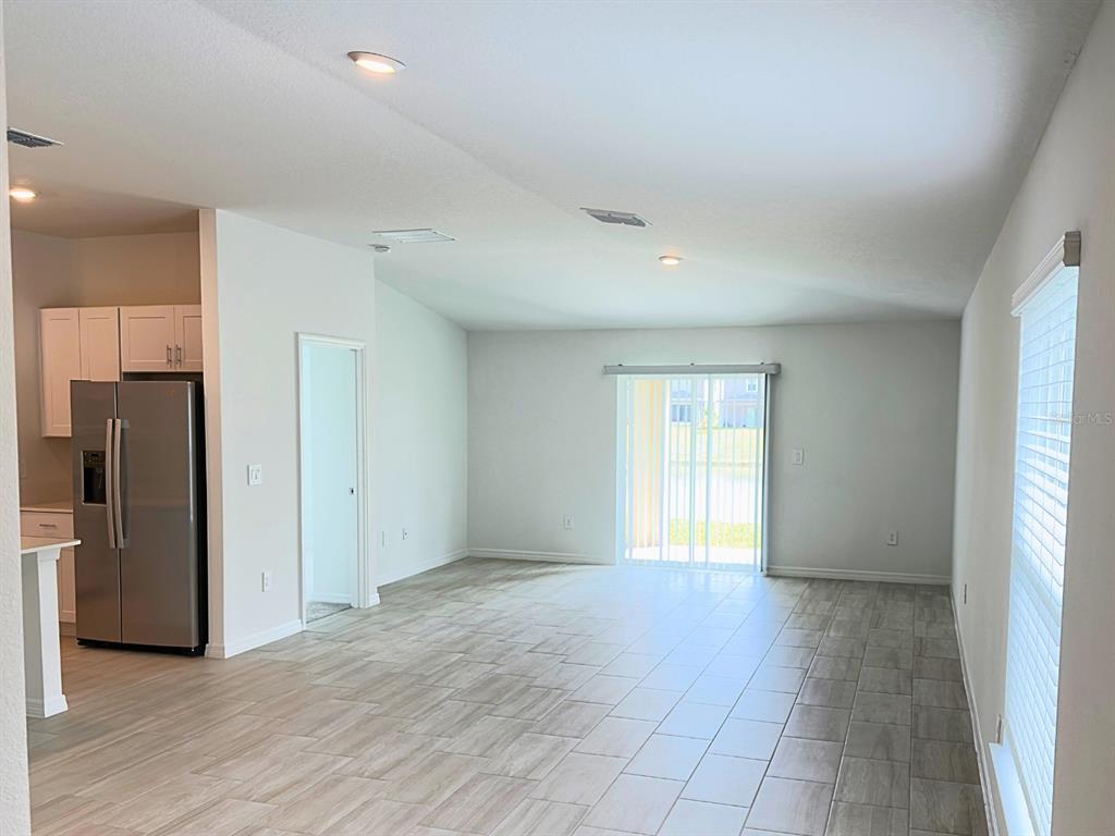An open-concept living area features light-colored tile flooring, a kitchen with stainless appliances, and sliding doors — 2318 ALLIUM ROSEUM LANE, PLANT CITY, FL
