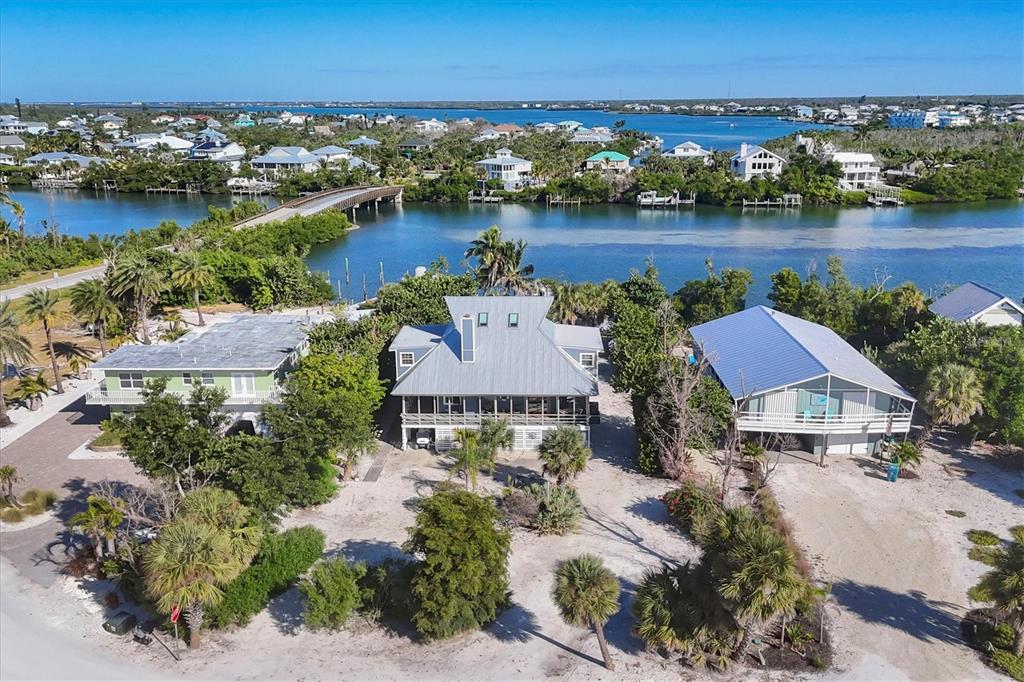 An aerial view shows three coastal houses surrounded by trees and sandy ground near water — 30 GASPARILLA WAY, PLACIDA, FL