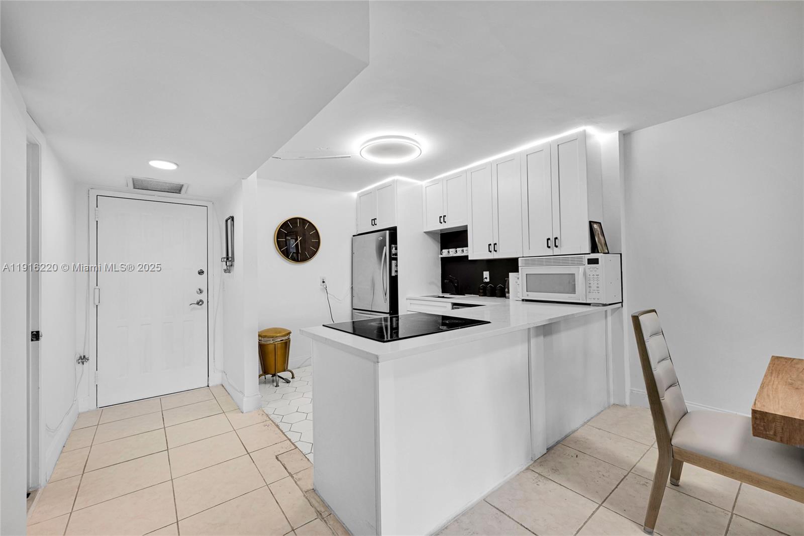 A white kitchen features a peninsula, stainless steel appliances, and a dining chair — 400 Leslie Dr # 605, Hallandale Beach FL 33009, HALLANDALE BEACH, FL