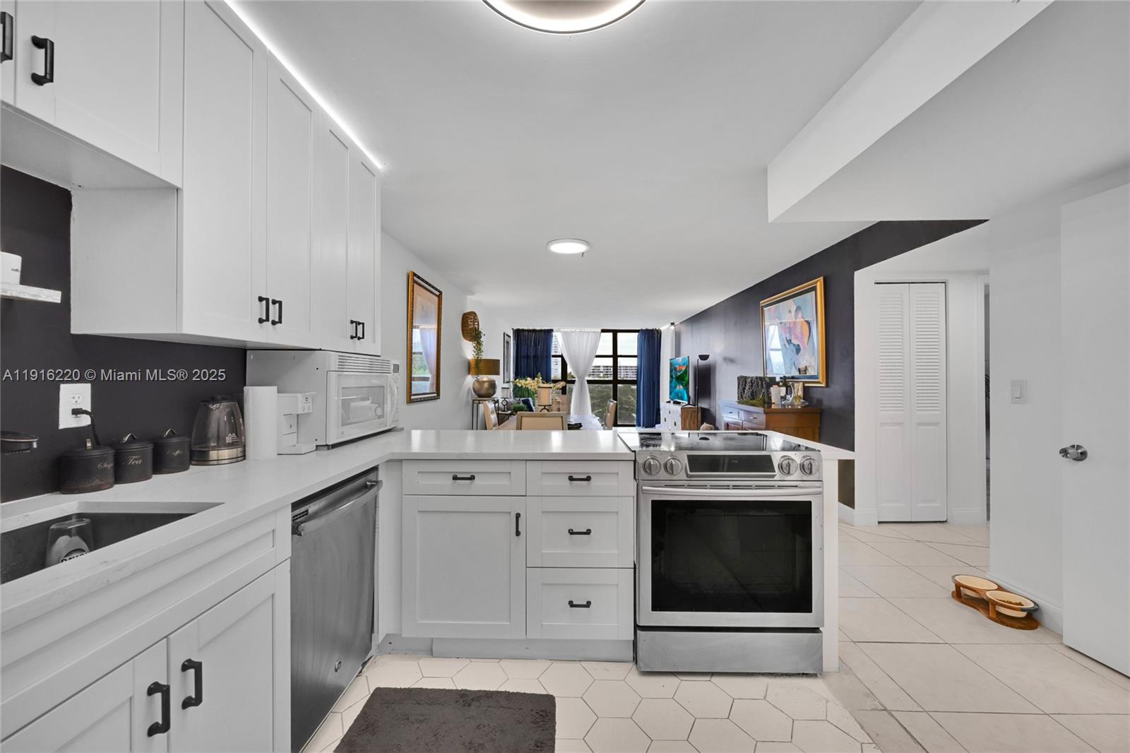 A kitchen with white cabinets, stainless steel appliances, and a peninsula overlooks a living area — 400 Leslie Dr # 605, Hallandale Beach FL 33009, HALLANDALE BEACH, FL