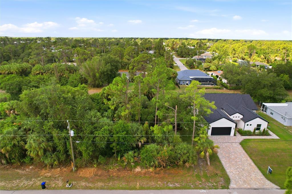 An aerial view shows a modern house with a paved driveway next to a wooded lot — OREGON LANE, NORTH PORT, FL
