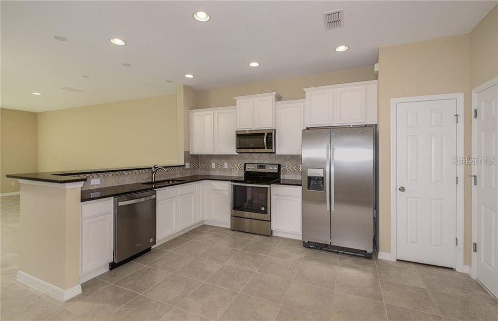 A kitchen with white cabinets, stainless steel appliances, and dark countertops on a tiled floor — 3890 GRASSLAND DRIVE, ORLANDO, FL