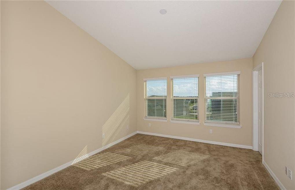 An empty bedroom with beige walls, brown carpet, and three windows with white blinds — 3890 GRASSLAND DRIVE, ORLANDO, FL
