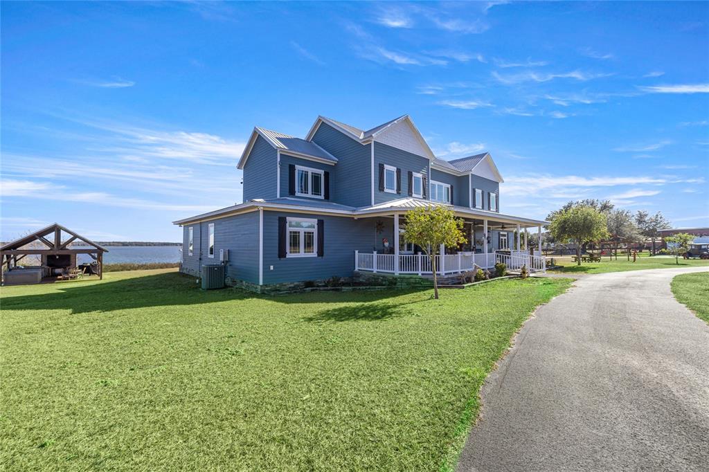 A blue two-story house with a wrap-around porch sits beside a lake and driveway — 5251 SE 180TH AVENUE ROAD, OCKLAWAHA, FL