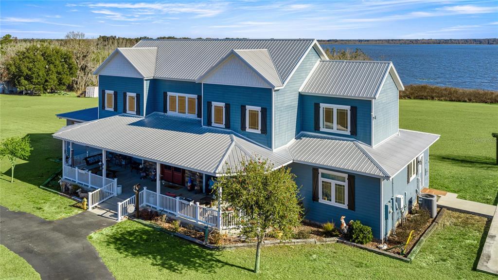 A blue two-story house with a metal roof and a wraparound porch sits near water — 5251 SE 180TH AVENUE ROAD, OCKLAWAHA, FL