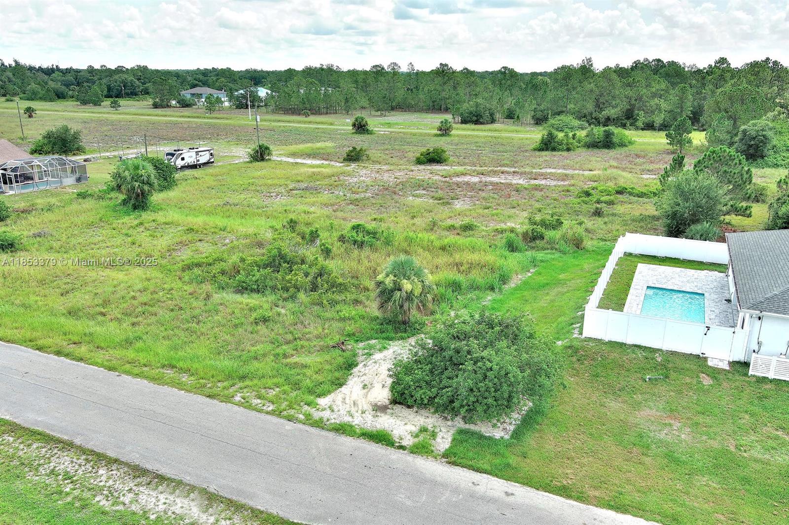 An aerial view shows a vacant grassy lot next to a house with a pool — 1502 ROOSEVELT AVE, Lehigh Acres FL 33972, LEHIGH ACRES, FL