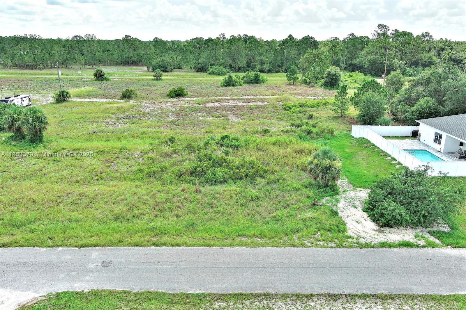 An aerial view shows a vacant, grassy lot next to a house with a pool — 1502 ROOSEVELT AVE, Lehigh Acres FL 33972, LEHIGH ACRES, FL