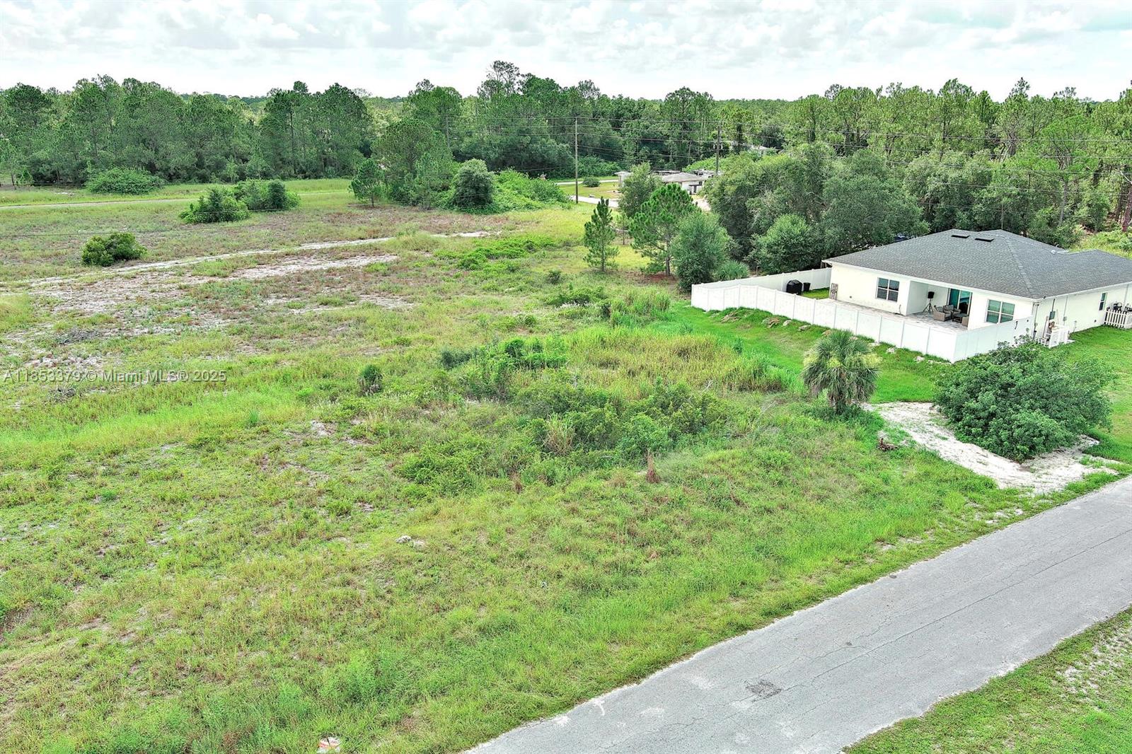 An aerial view shows a large, grassy vacant lot next to a single-story residential home — 1502 ROOSEVELT AVE, Lehigh Acres FL 33972, LEHIGH ACRES, FL