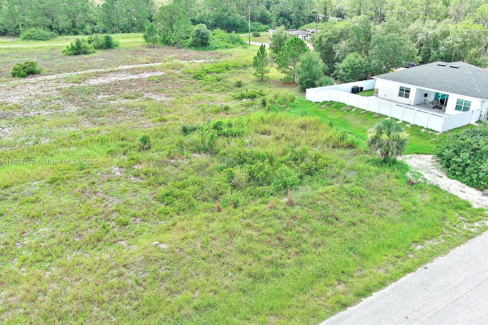An aerial view shows a vacant, grassy lot adjacent to a house with a white fence — 1502 ROOSEVELT AVE, Lehigh Acres FL 33972, LEHIGH ACRES, FL