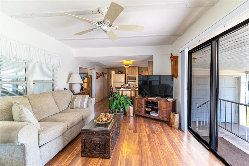 A living room with wood-look flooring, a beige sofa, a television, and a ceiling fan — 107 EDGEWOOD BOULEVARD, LAKE WALES, FL