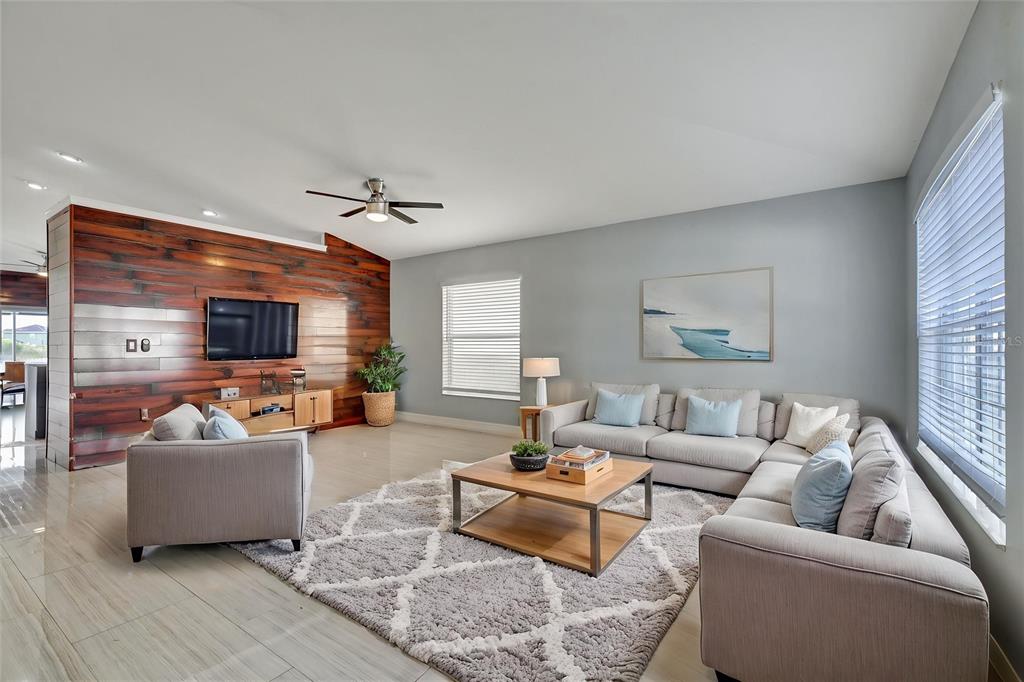 A living room features a wood-paneled accent wall, a sectional sofa, and a patterned rug — 8105 TAR HOLLOW DRIVE, GIBSONTON, FL
