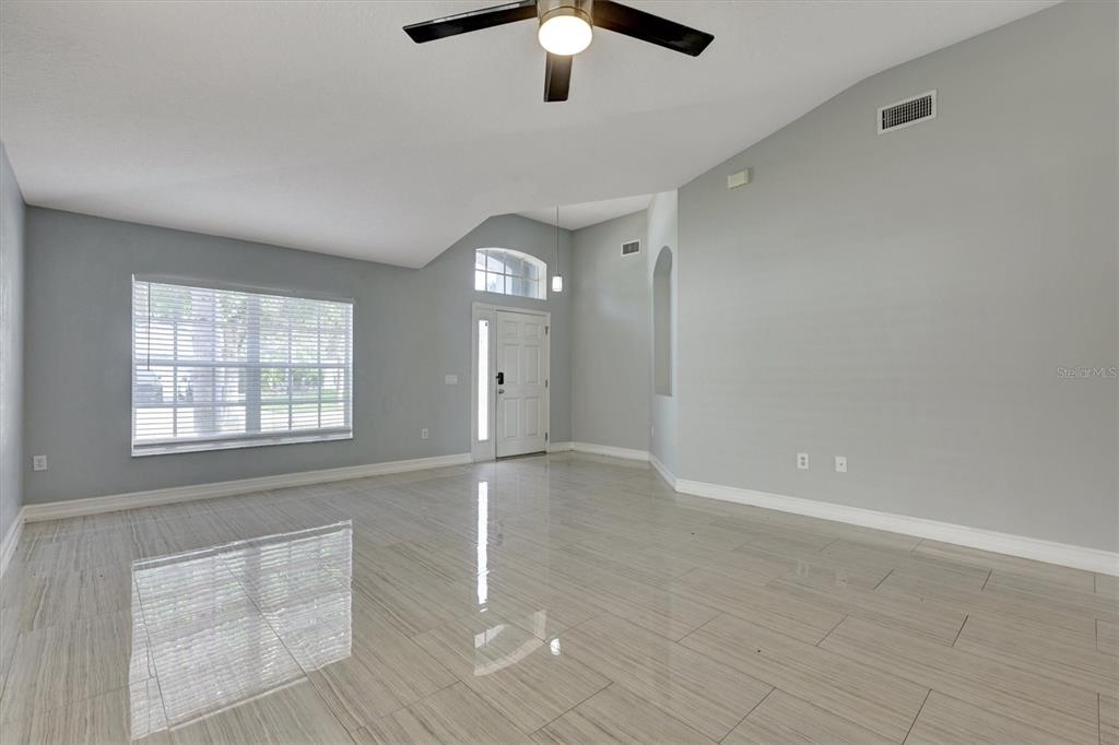 A bright living room features light gray walls, large windows, and glossy tile flooring — 8105 TAR HOLLOW DRIVE, GIBSONTON, FL