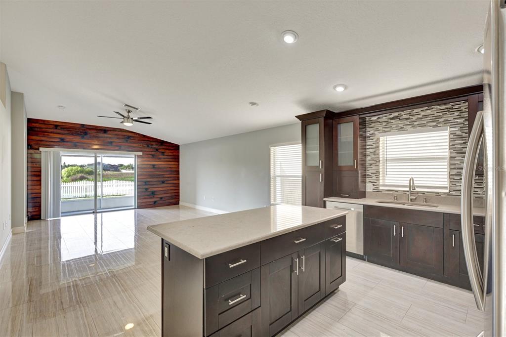 A kitchen with dark cabinets and a stone island overlooks a living area with wood-paneled walls — 8105 TAR HOLLOW DRIVE, GIBSONTON, FL