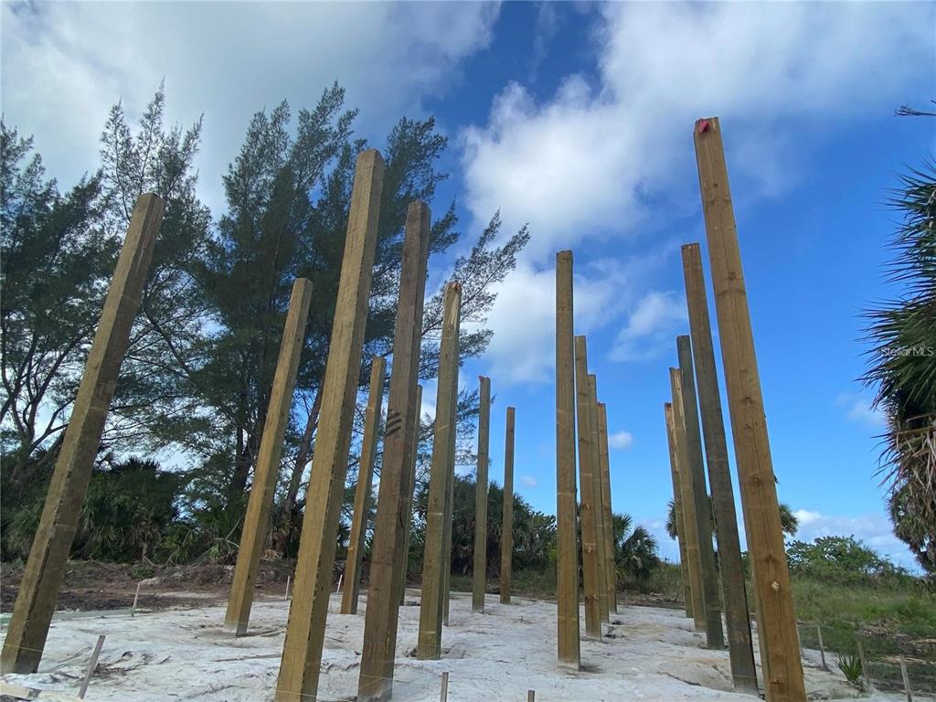 A construction site features several tall wooden support posts standing on a sandy lot — 500 S GULF BOULEVARD, PLACIDA, FL