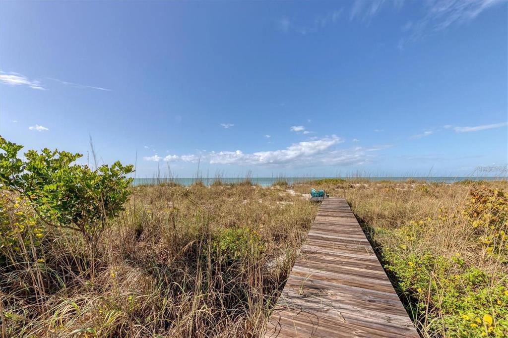 A wooden boardwalk leads through beach grass toward the ocean under a blue sky — 500 S GULF BOULEVARD, PLACIDA, FL