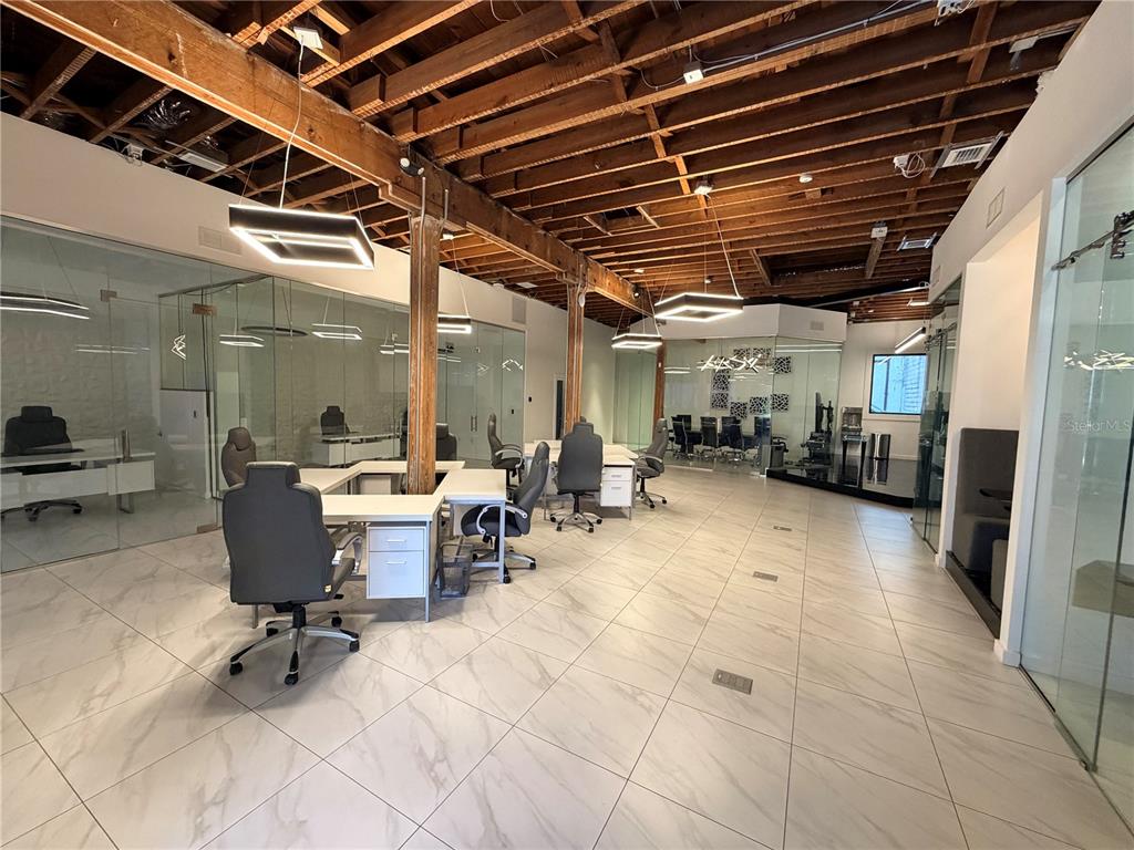 An open-plan office space features glass-walled cubicles, marble-look tile flooring, and exposed wooden ceiling beams — 1006 N FLORIDA AVENUE, TAMPA, FL