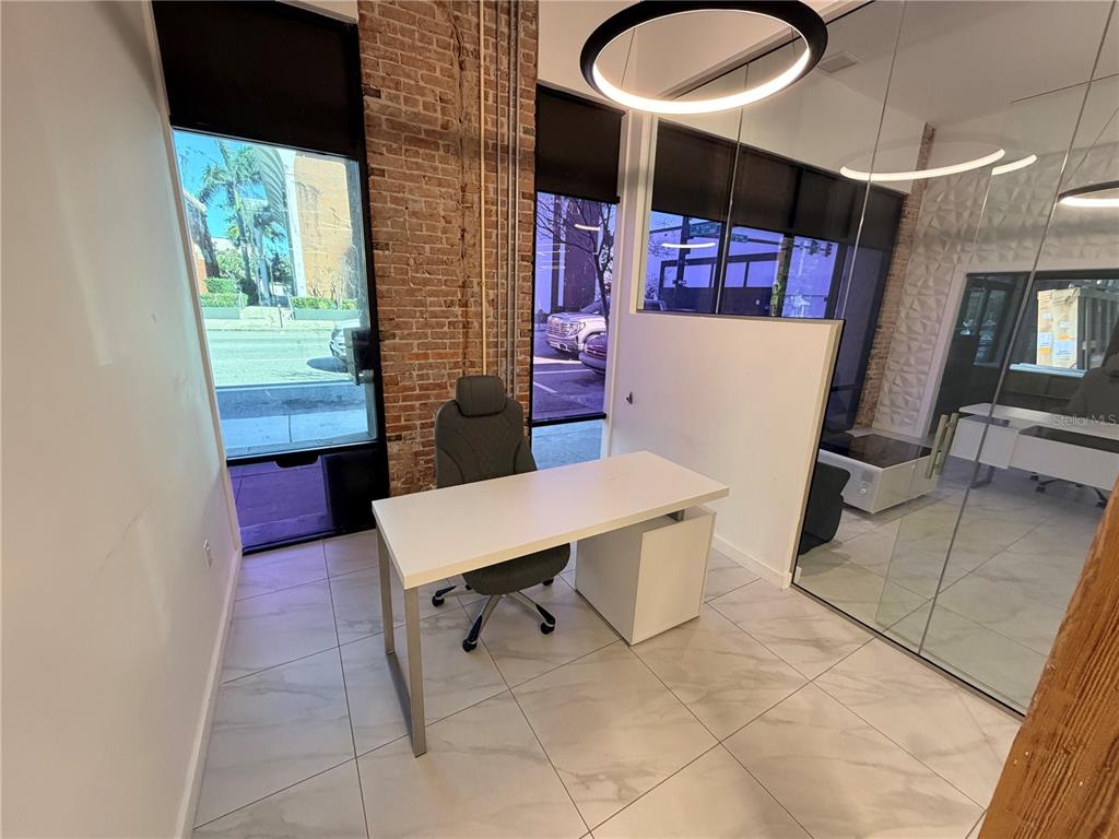 A modern office space features a white desk, grey chair, exposed brick, and glass walls — 1006 N FLORIDA AVENUE, TAMPA, FL