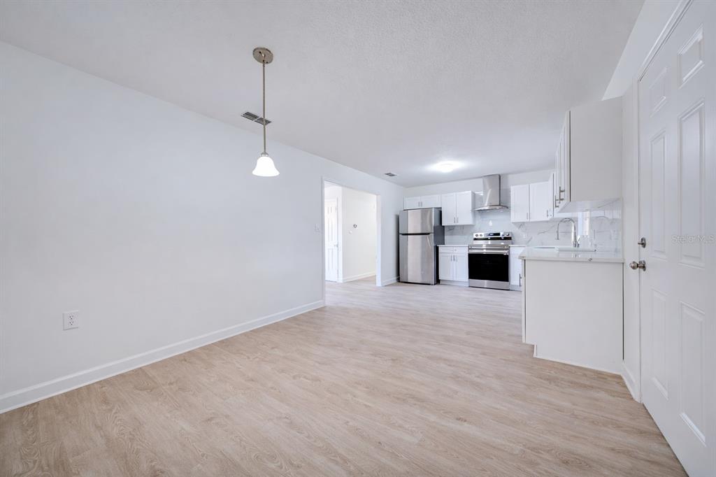 A bright, open-concept kitchen and dining area featuring white cabinetry, stainless steel appliances, and wood-look flooring — 720 SWISS DRIVE, LAKELAND, FL