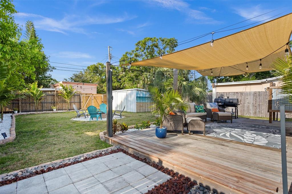 A backyard features a wooden deck with a shade sail, patio furniture, and a fire pit — 1018 55TH AVENUE N, ST PETERSBURG, FL