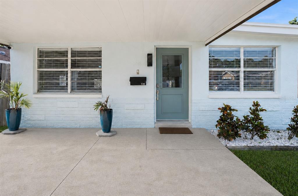 A light blue house exterior features a covered concrete porch, a teal door, and windows — 1018 55TH AVENUE N, ST PETERSBURG, FL
