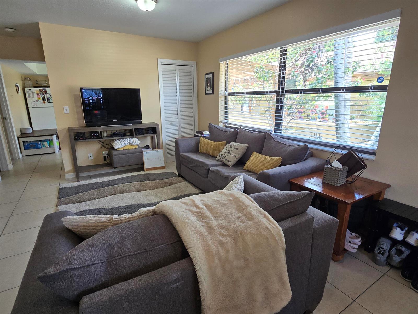 A living room features a grey sectional sofa, a television on a console, and large windows — 1155 White Pine Pine # 1155, Wellington FL 33414, WELLINGTON, FL