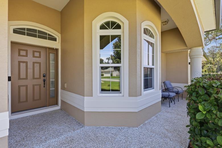 The front entrance features a tan door, arched windows, and a covered porch with chairs — 69 WELLESLEY LANE, PALM COAST, FL, FL