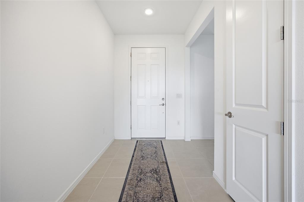 A bright entryway features white walls, tile flooring, a runner rug, and a white door — 6064 SW 86TH TERRACE ROAD, OCALA, FL
