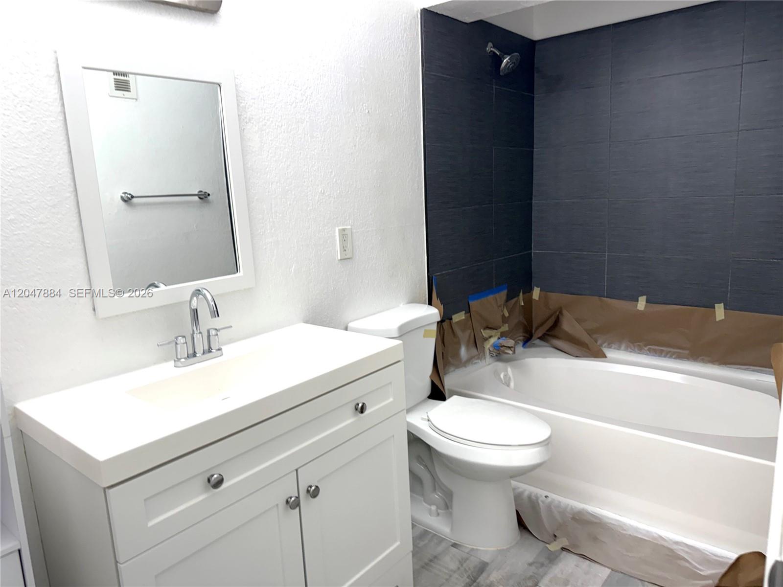 A bathroom features a white vanity, a toilet, and a bathtub with dark tiled walls — 15560 SW 104th Ter # 619, Miami FL 33196, MIAMI, FL