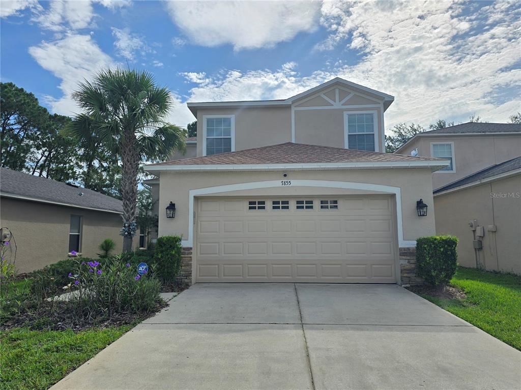 A two-story house with a beige stucco exterior, a two-car garage, and a palm tree — 7855 TUSCANY WOODS DRIVE, TAMPA, FL