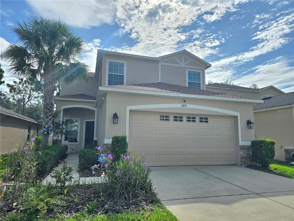 A two-story suburban house features a tan stucco exterior, a two-car garage, and landscaping — 7855 TUSCANY WOODS DRIVE, TAMPA, FL