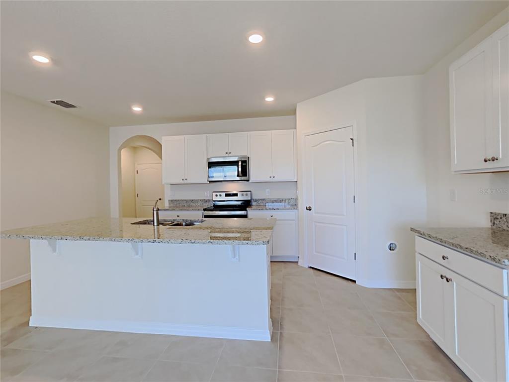 A kitchen features white cabinets, granite countertops, a center island, and tile flooring — 9678 BLACK WALNUT DRIVE, CLERMONT, FL