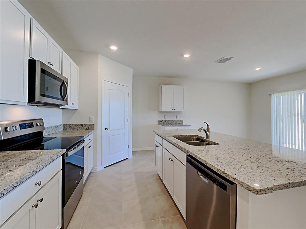 A kitchen features white cabinets, granite countertops, stainless steel appliances, and a central island — 9678 BLACK WALNUT DRIVE, CLERMONT, FL