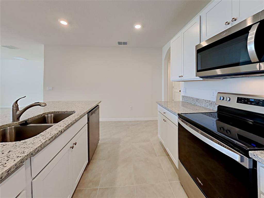 A kitchen features white cabinets, granite countertops, stainless steel appliances, and tile flooring — 9678 BLACK WALNUT DRIVE, CLERMONT, FL