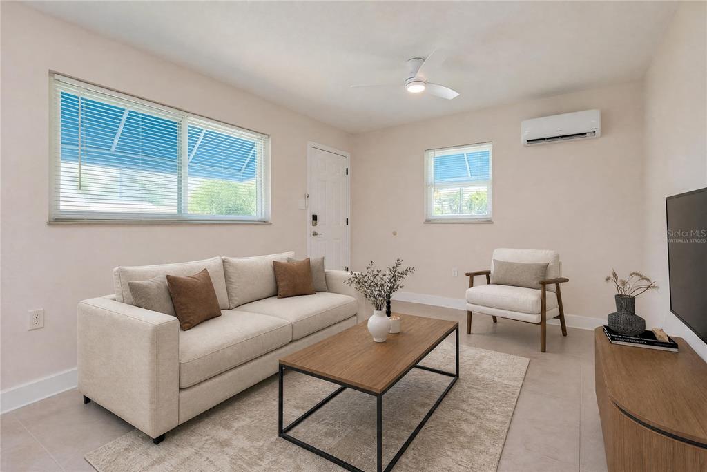 A living room with a sofa, coffee table, armchair, and a wall-mounted air conditioning unit — 190 73RD AVENUE UNIT A, ST PETE BEACH, FL