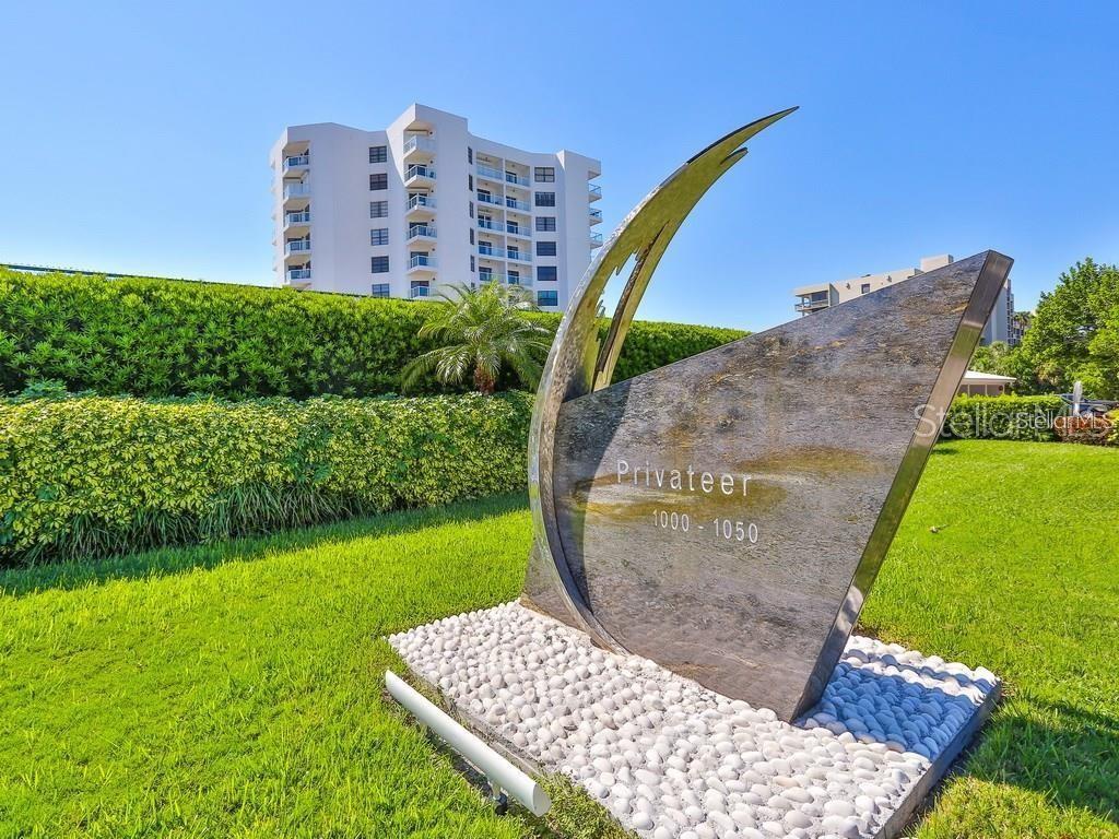 A stone monument with the name Privateer stands on a lawn before a tall building — 1050 LONGBOAT CLUB ROAD UNIT 502, LONGBOAT KEY, FL