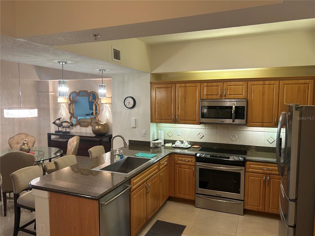 A kitchen with wood cabinets, granite countertops, and stainless steel appliances overlooks a dining area — 200 OCEAN CREST DRIVE UNIT 118, PALM COAST, FL