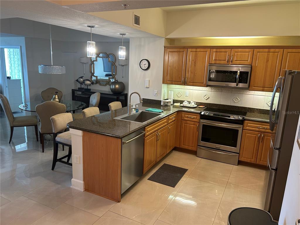 A kitchen with wood cabinets, granite countertops, and stainless steel appliances overlooks a dining area — 200 OCEAN CREST DRIVE UNIT 118, PALM COAST, FL