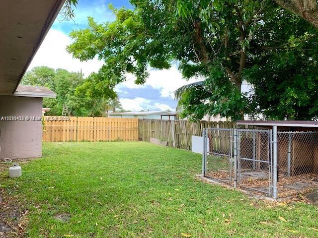 A grassy backyard features a wooden fence, a chain-link dog kennel, and large trees — 6720 NW 28th St, Sunrise FL 33313, SUNRISE, FL