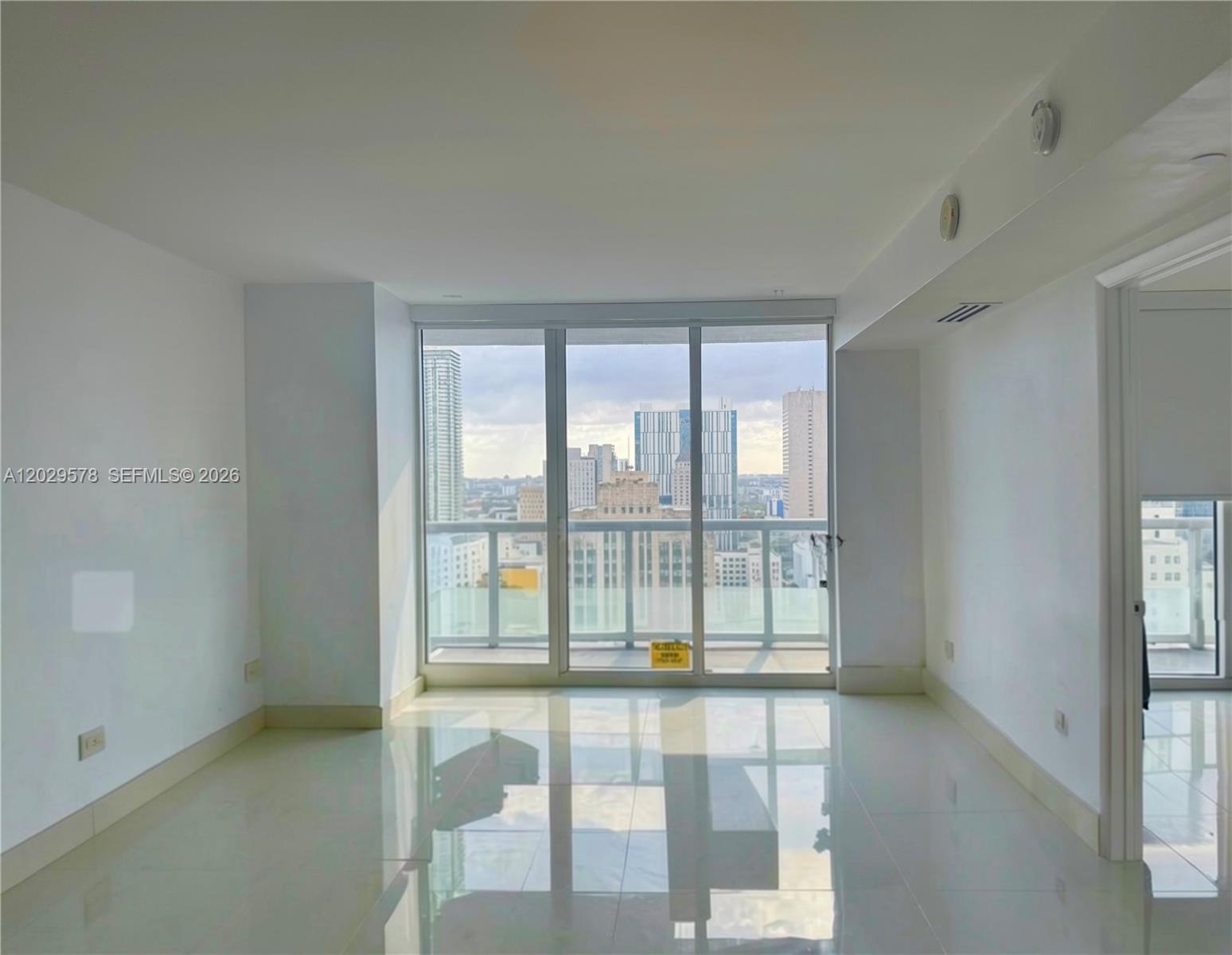 An empty room with white walls, glossy tile floors, and a balcony overlooking city buildings — 50 Biscayne Blvd # 2707, Miami FL 33132, MIAMI, FL