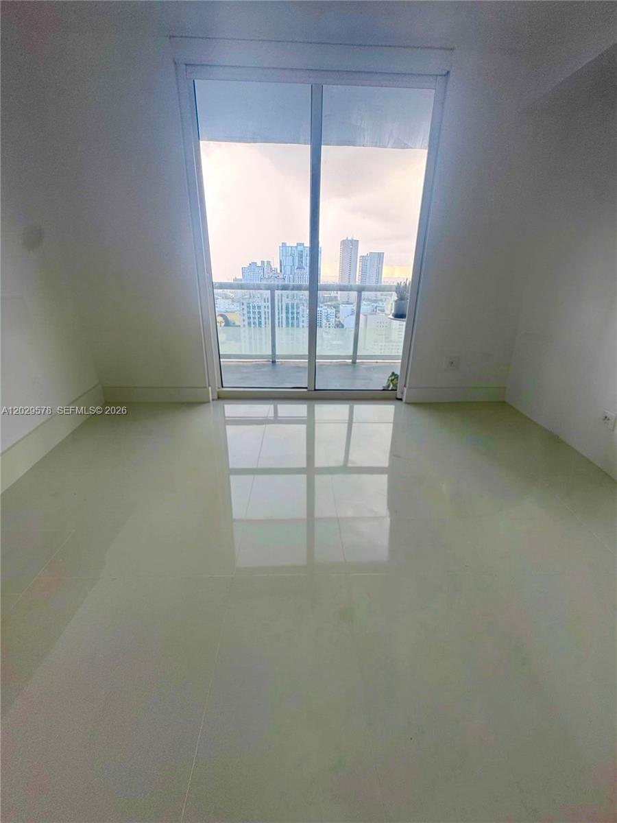 An empty room with light-colored tile flooring and a sliding glass door to a balcony — 50 Biscayne Blvd # 2707, Miami FL 33132, MIAMI, FL