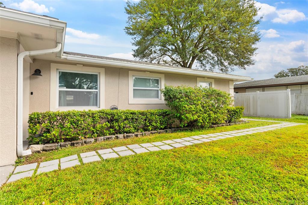 A beige house exterior features a stone-lined hedge, white window frames, and a stone walkway — 1019 SUSAN DRIVE, LAKELAND, FL