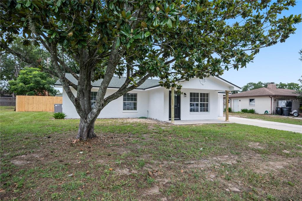 A white brick house with a large tree in the front yard and a porch — 4052 LANA DRIVE, LAKELAND, FL