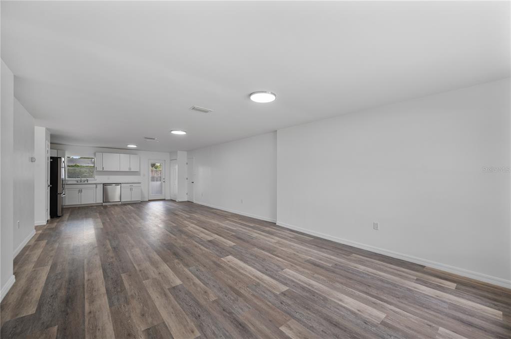 An open-concept room features white walls, recessed lighting, and wood-look flooring with a kitchen area — 4052 LANA DRIVE, LAKELAND, FL
