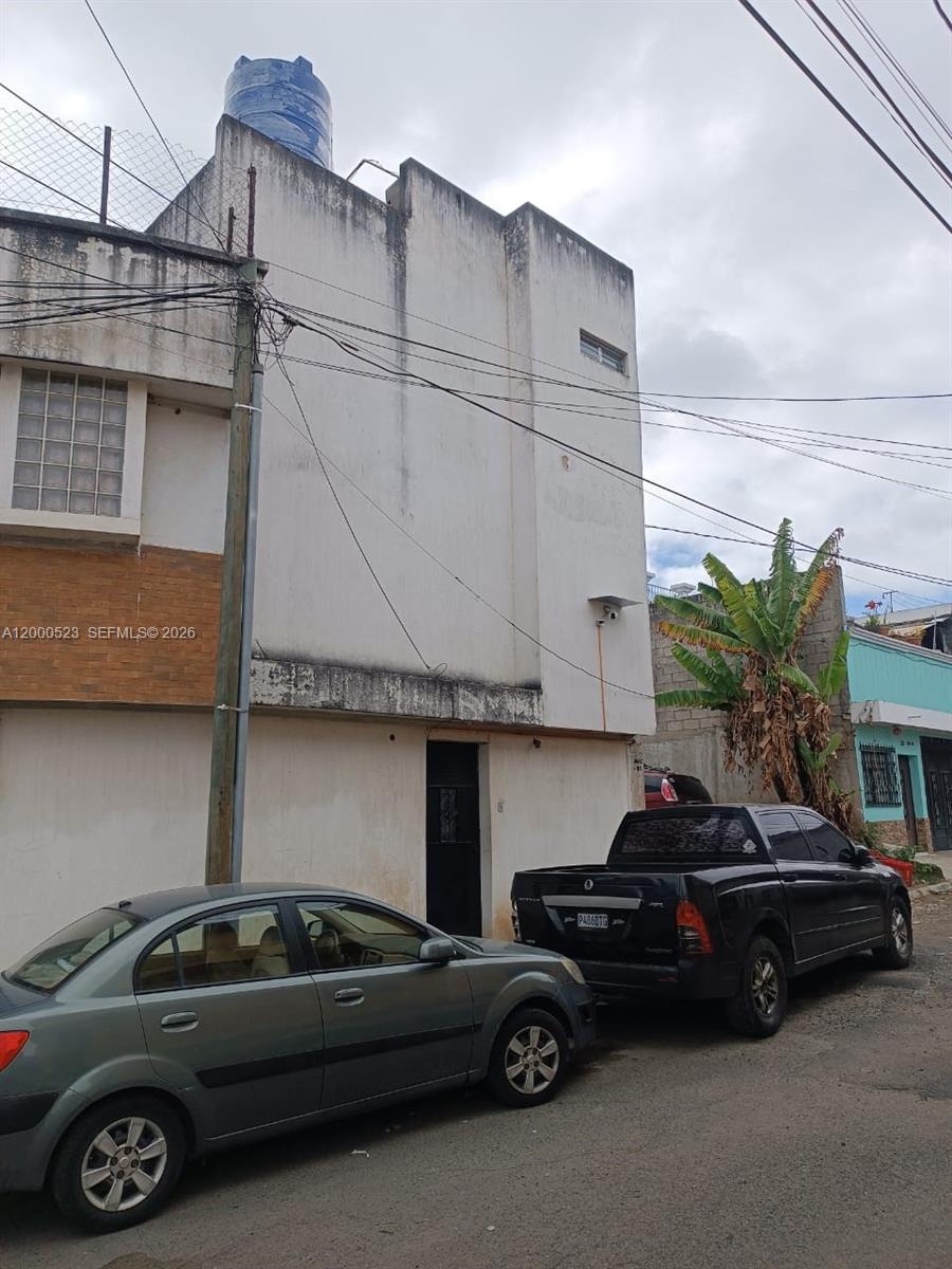 A two-story white building with a water tank on the roof sits beside parked cars — 9 calle NW 8-92 zona 11, MA 01057, MA