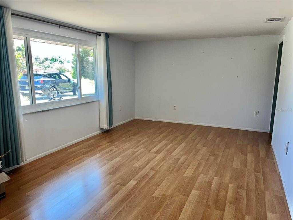 An empty room features light-colored walls, wood-look flooring, and a large window with curtains — 503 S VENICE BOULEVARD, VENICE, FL