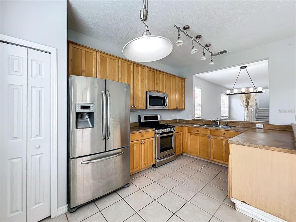 A kitchen with light wood cabinets, stainless steel appliances, and beige tile flooring — 5356 WATERVISTA DRIVE, ORLANDO, FL
